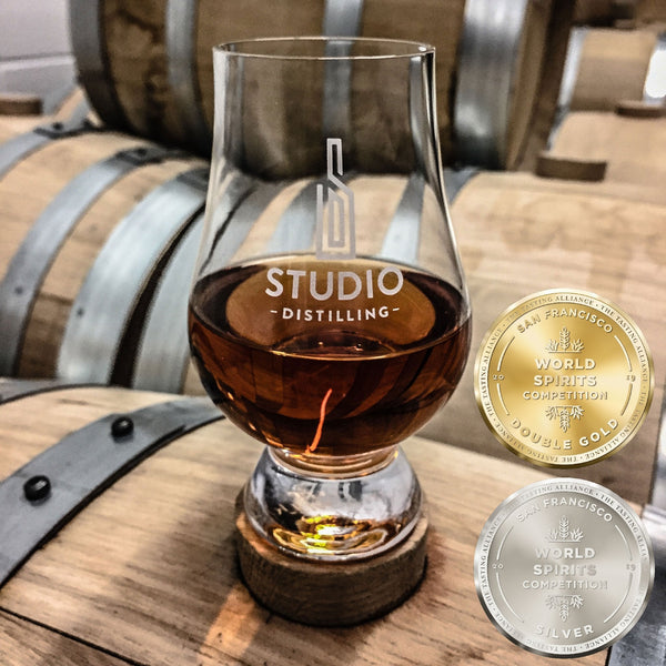 Sample galss of Studio Distilling Bourbon on a barrel with medals